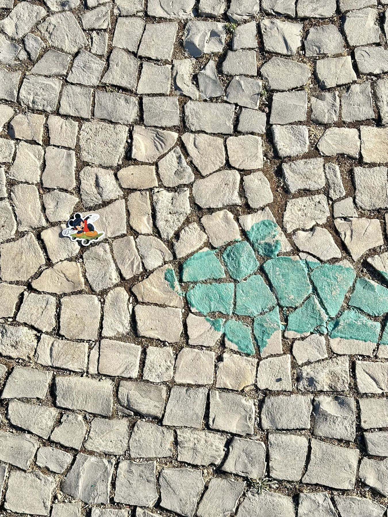 Portugiesisches Pflaster mit einem türkisfarbenen Herz und einem Mickey-Mouse-Sticker — Straße in Lissabon